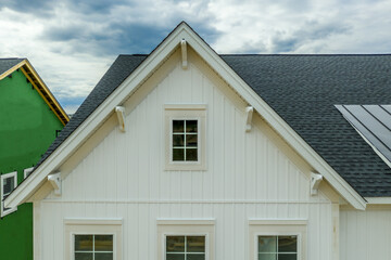Elegant white gable with attic window, brackets, vertical vinyl lap siding with cloudy sky American...