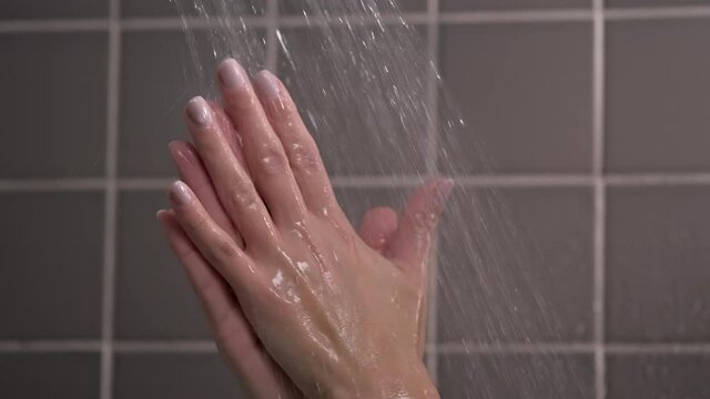 Woman in the bathroom and the shower washes her hands. Drops of water flow through the hands. Care for the same and health. Routine procedures.