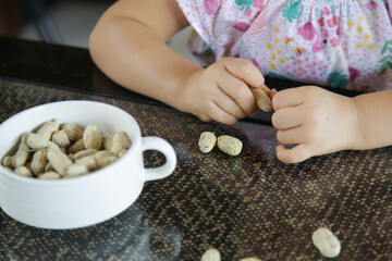 Toddler girl eating peanuts in shell on the kitchen table