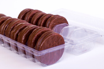 Chocolate covered biscuits lined up in a transparent box on white with copy space