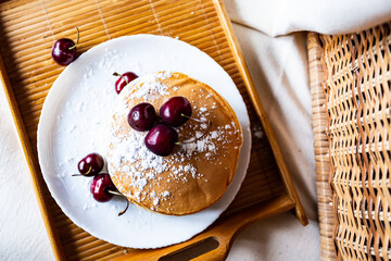 Pancakes with cherries on a white plate on a wooden background