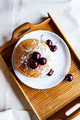 Pancakes with cherries on a white plate on a wooden background