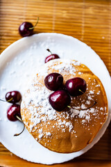 Pancakes with cherries on a white plate on a wooden background
