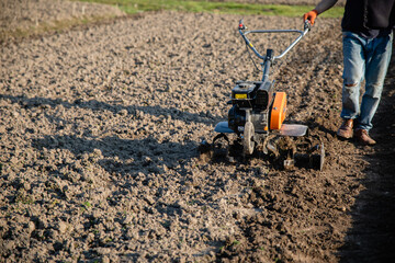 small orange plowing machine in hands of a farmer making arable in black soil