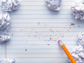 School supplies of blank lined notebook paper with eraser marks and erased pencil writing, surrounded by balled up paper and a pencil eraser. Studying or writing mistakes concept.