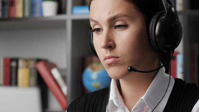 Woman is talking on video link. Serious girl in headphones looks at monitor screen, she communicates on video connection, basically agreeing with interlocutor. Online learning, remote work concept