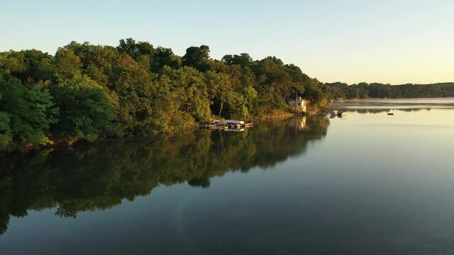 Aerial view of rural landscape with lush greenery and lake at dawn. The shoreline with boat docks. American Midwestern countryside scenery in the early sunny morning. The camera moves forward