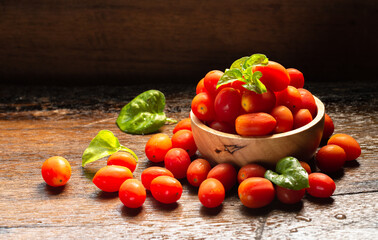 Small red fresh tomatos in wood bowl on wood table with nature light.