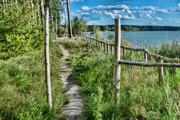 Fototapeta na wymiar rustic wooden fence on shore of river at sunny day 