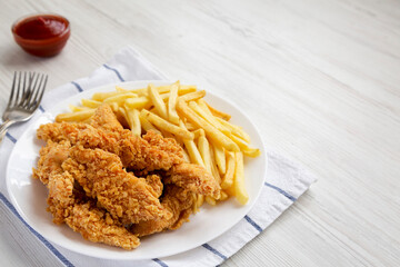 Homemade Crispy Chicken Tenders and French Fries on a white plate, side view. Space for text.