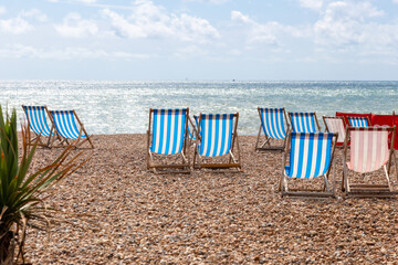 Colourful striped empty deck chairs for rent on the pebble beach at Brighton, East Sussex, England