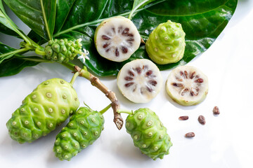 Naklejka na ściany i meble Noni fruit or Morinda Citrifolia and noni slice with seed and green leaves of the noni isolated on white background.