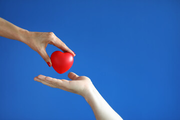 Female hand give red heart to male hand on blue background close-up. Professional diagnosis and...