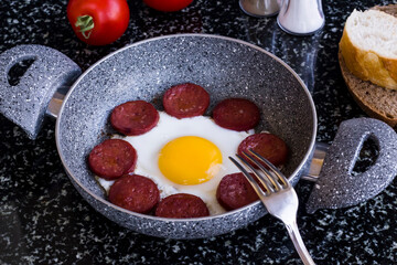 Egg with sausage in egg pan on granite marble table with a fork,top view and flat layout.