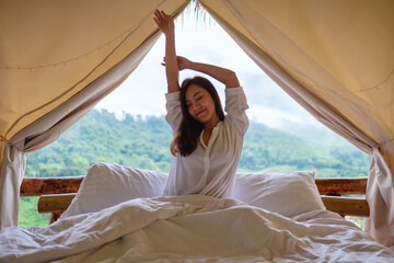 Portrait image of a woman do stretching after waking up in the morning with a beautiful nature view outside the tent