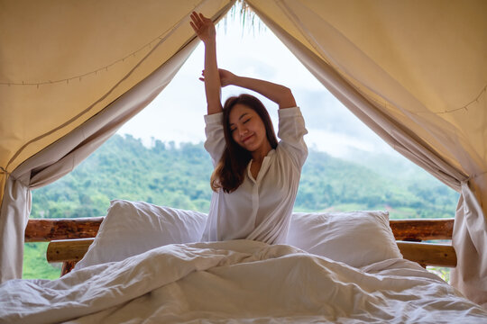 Portrait image of a woman do stretching after waking up in the morning with a beautiful nature view outside the tent