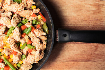 Fried tender chicken pieces with vegetable mixture in pan on wooden board.
