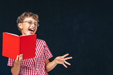 funny smiling boy with glasses and book in his hand, posing on black background.