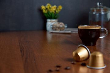 Transparent cup of espresso coffee, golden capsules and roasted beans on a brown rustic wooden table. Caffeine, hot drinks and objects concept. Front view.