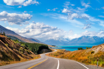  Spectacular winding road at Lake Pukaki, a glacial alpine lake in New Zealand's South Island, one of the iconic tourist destinations, on a summer day with snow-capped mountain in fog in the distance.