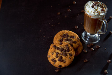 Close up of a glass cup of coffee with whipped cream and chocolate on it, chocolate chip cookies...