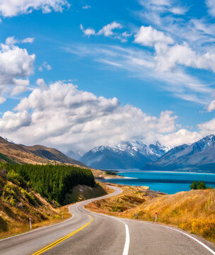Vertical panorama of the winding road along Lake Pukaki in New Zealand's South Island, one of the iconic destinations, set in a glacier-carved valley surrounded by snow-capped mountain peaks.