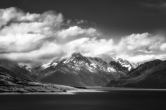 Dramatic alpine view in black and white of snow-capped Mount Cook engulfed in clouds, on the shore of Lake Pukaki, in New Zealand, South Island, on a beautiful summer day.