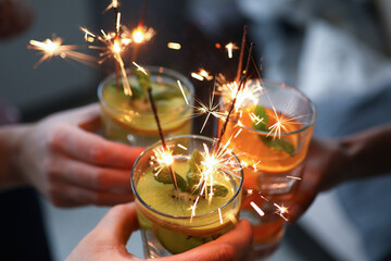 Three hands hold three glasses with cocktail and sparklers close-up. In glass alcohol is poured...