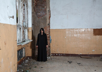 young goth woman stands in the room of an abandoned house