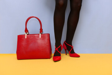 Girl feet with red high heels and red bag isolated on blue and yellow saturated background
