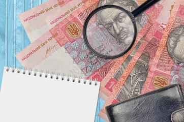 10 Ukrainian hryvnias bills and magnifying glass with black purse and notepad. Concept of...