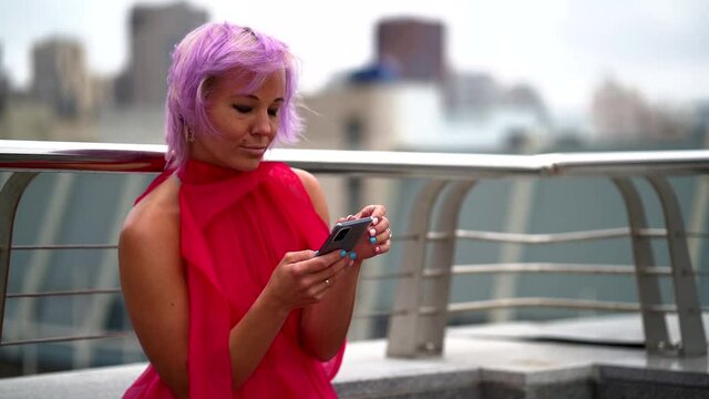 extravagant woman with purple hair is viewing social nets and watching pictures in smartphone