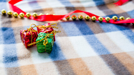 New Year and Christmas card. Christmas decoration plaid in a cage. Three small gifts, gold beads and a red satin ribbon lie on a winter blanket. Place for your text. Copy space. Selective focus.