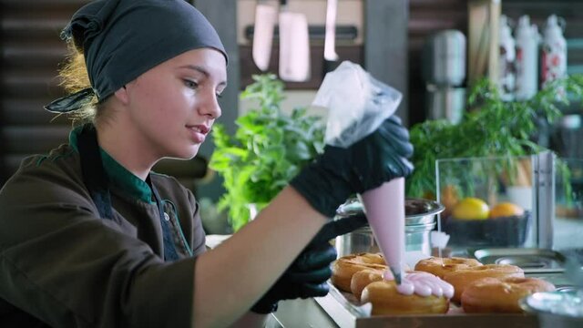 dessert, handsome professional chef confectioner in gloves, squeezes thick protein cream from pastry bag to decorate delicious fresh donuts, unhealthy food