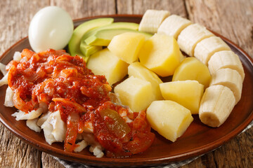 Delicious Bermuda breakfast made from salted cod with onion tomato sauce, boiled potatoes, eggs, banana and avocado close-up in a plate. horizontal