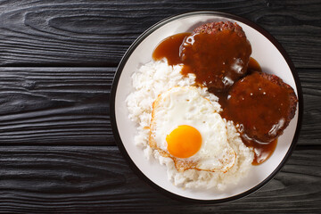 Loco Moco recipe is a delicious Hawaiian dish consists of white rice, a juicy hamburger patty, a fried egg, and brown gravy close-up on a plate. Horizontal top view