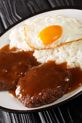 Loco moco is a dish featured in contemporary Hawaiian cuisine consists of white rice, topped with a hamburger, a fried egg, and brown gravy  close-up on the table. Vertical