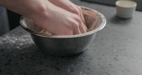 man mixing dough in steel bowl on concrete countertop