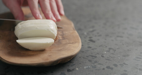 man slicing fresh mozzarella cheese on olive wood board