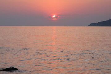 Pale pink sunset at the seaside. Seascape sunset on the sea, the sky and the water surface are pink, the sun hides behind a cloud on the horizon