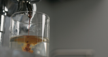 low angle pour from coffee machine into glass with water
