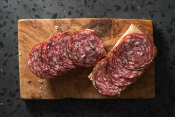 Ciabatta slices with slices of salami sausage on olive wood board