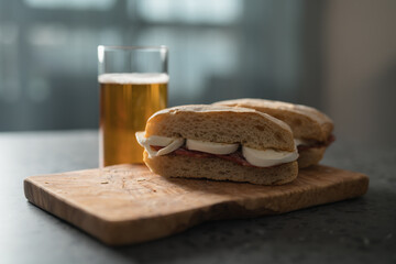Fototapeta na wymiar Ciabatta sandwiches with salami and mozzarella on olive wood board next to glass of beer