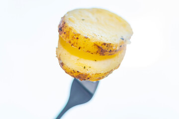 Hot baked potatoes with thin-skinned slices. A piece of potatoes on a fork on a white background. A simple and quick after-work meal for the worker and bachelor. Inexpensive food