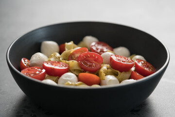 fettuccine pasta with pesto, mozzarella and cherry tomatoes in black bowl on concrete background