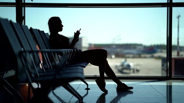 female passenger in waiting area of airport, wait for flight, surfing internet