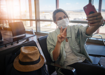 Young woman traveler in a protective medical mask with a backpack sits in the waiting room and...
