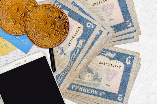 5 Ukrainian hryvnias bills and golden bitcoins with smartphone and credit cards. Cryptocurrency investment concept. Crypto mining or trading
