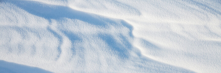 Beautiful winter background with snowy ground. Natural snow texture. Wind sculpted patterns on snow surface. Wide panoramic texture for background and design.