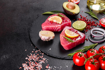 Fresh tuna fillet steaks with spices and herbs on a black background